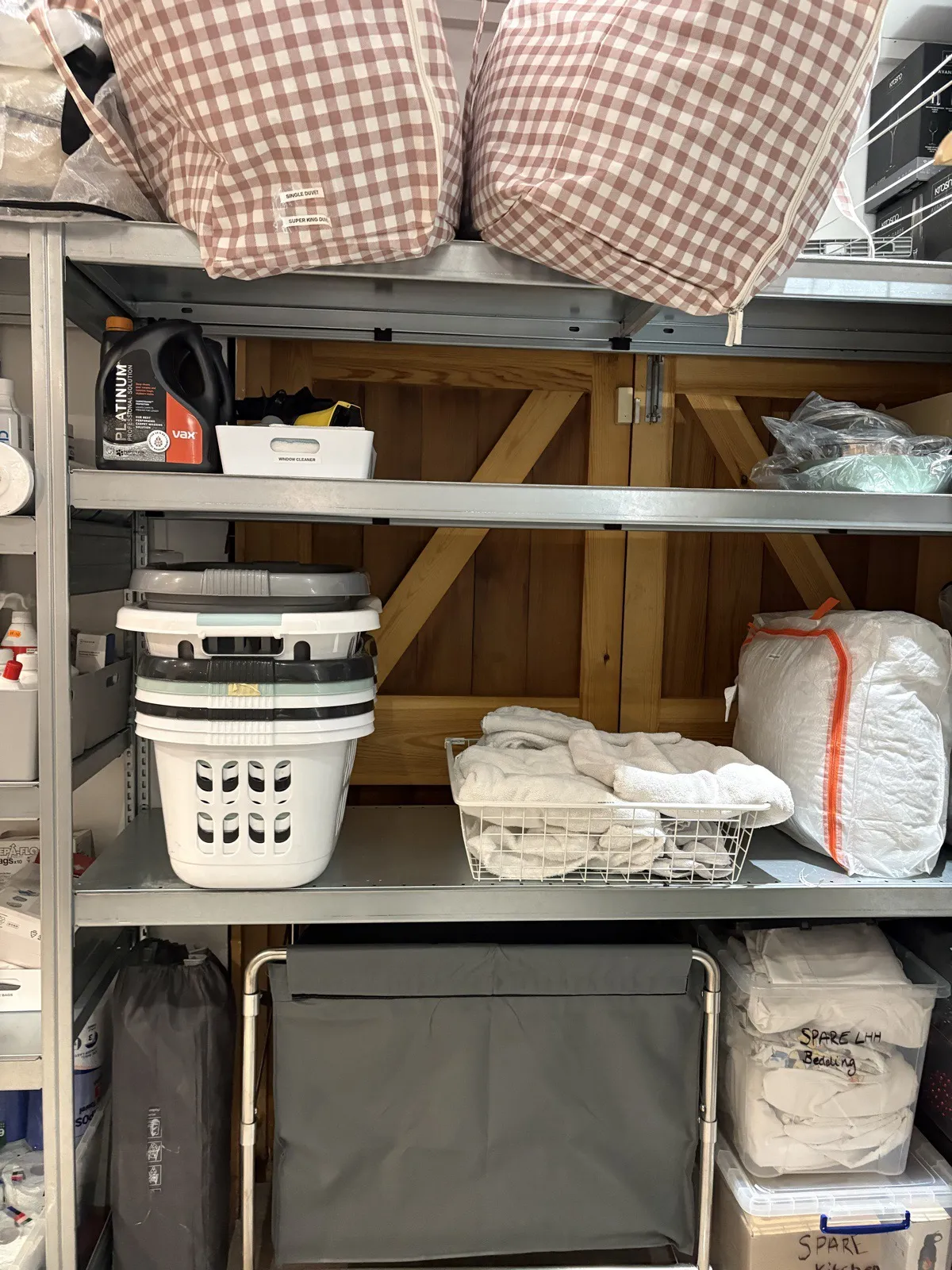 A metal shelving unit with laundry baskets, folded towels and labelled bedding boxes