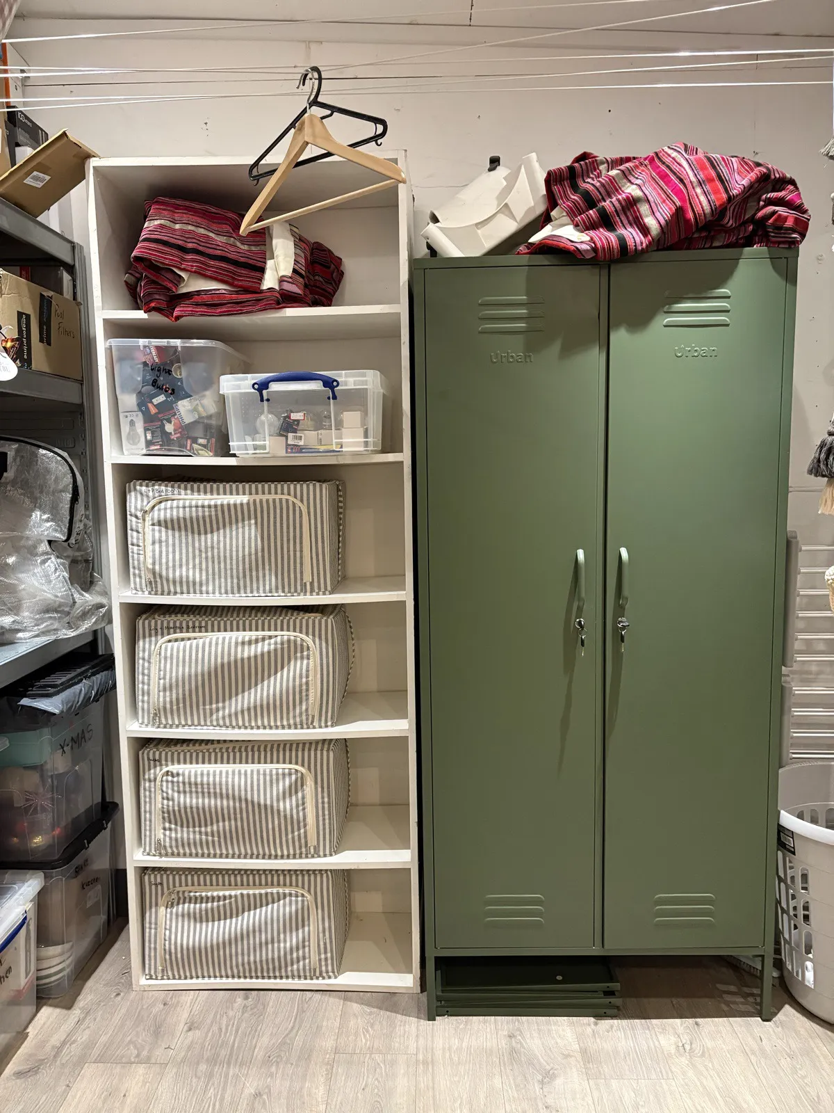 A white bookcase with striped storage boxes next to a green metal locker